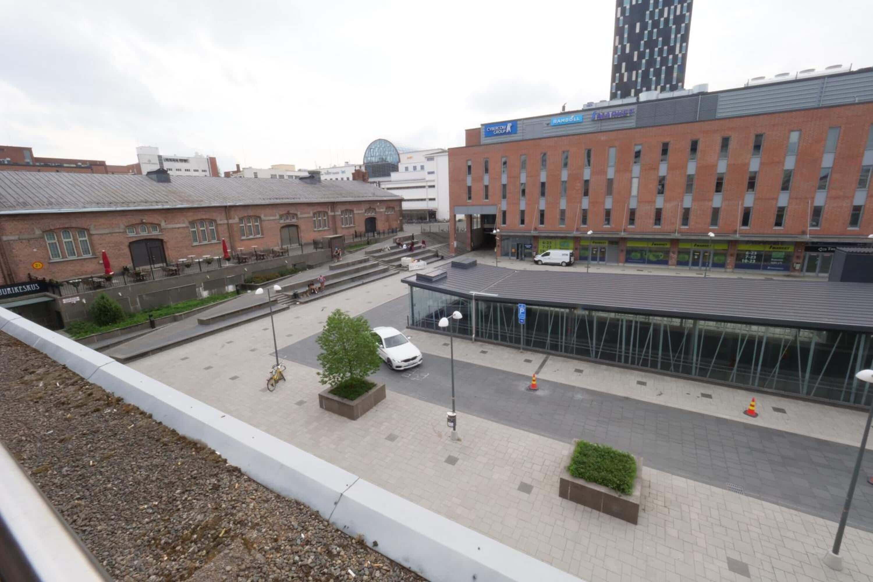 A modern building with a glass facade, a parking area with a white car, and a brick building in the background.