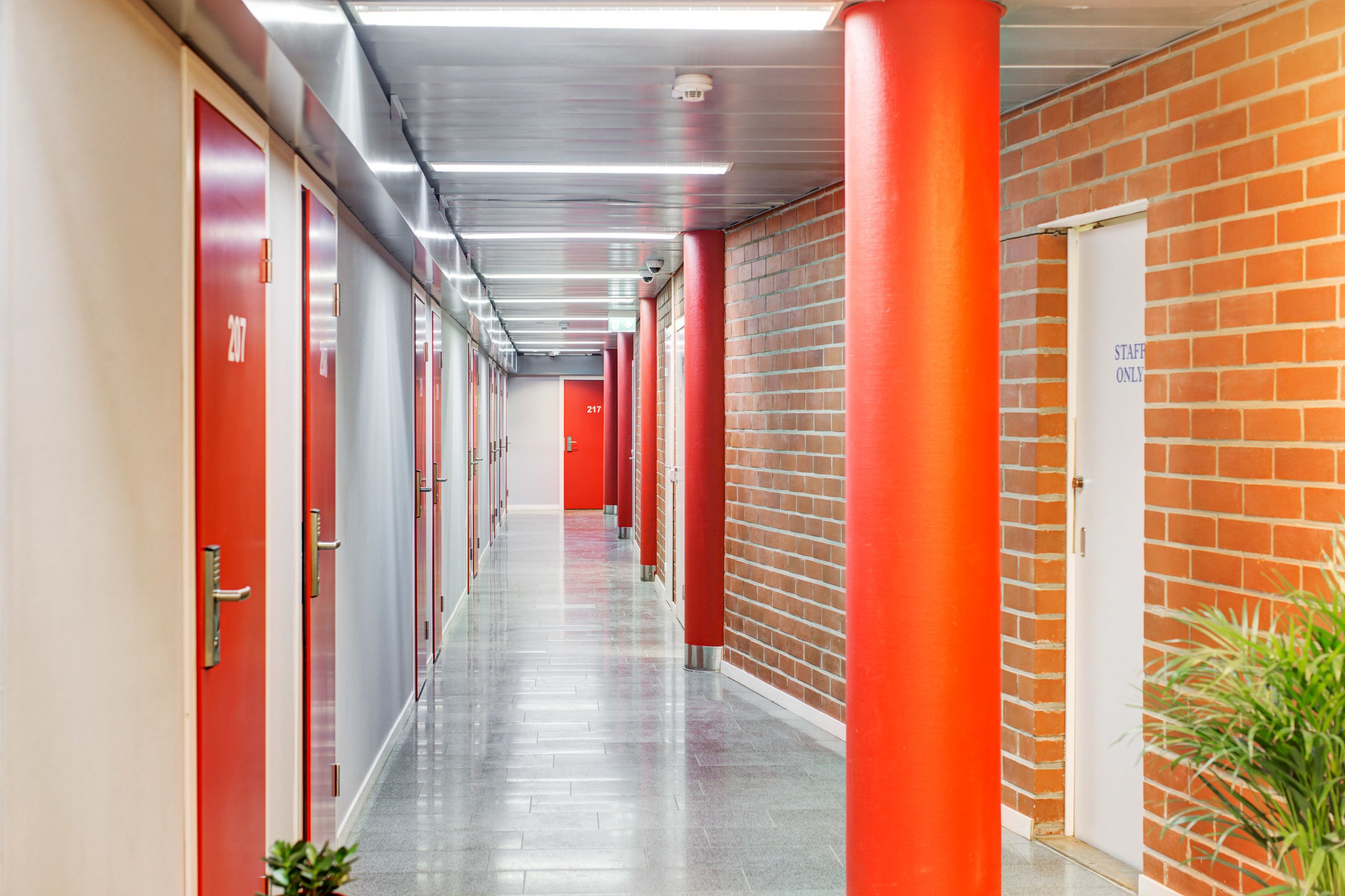 A long corridor with red doors, a brick wall, and a white door labeled "STAFF ONLY".