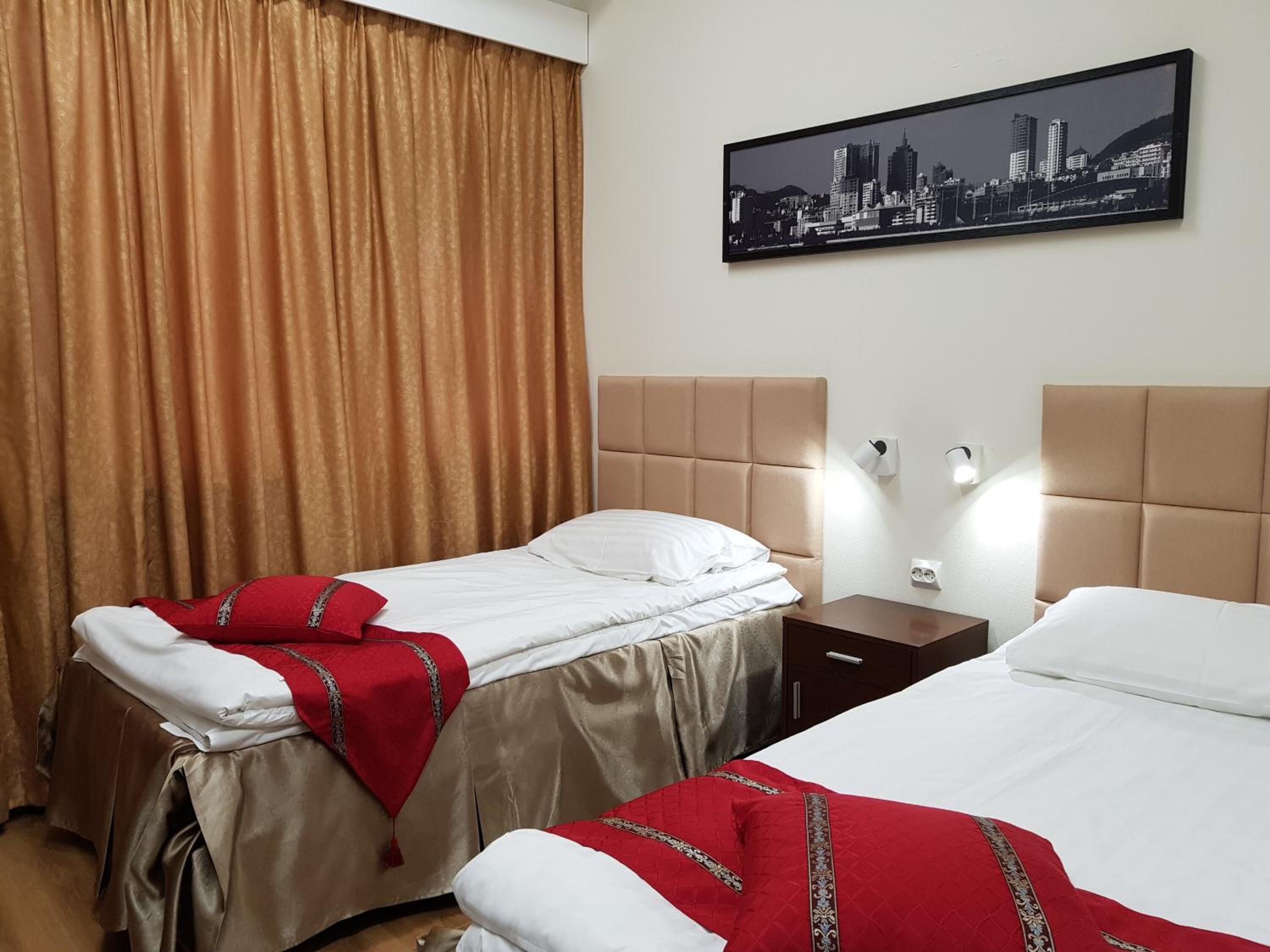 A hotel room with two beds, a cityscape view, a curtain, and a nightstand with a lamp.
