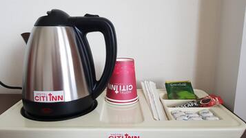 A hotel minibar setup with a kettle, a red cup, a green tea box, and a tray with snacks.