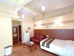 Una habitación de hotel con una cama, un sofá de cuero rojo, una mesita de madera, un radiador blanco y un aplique de pared.