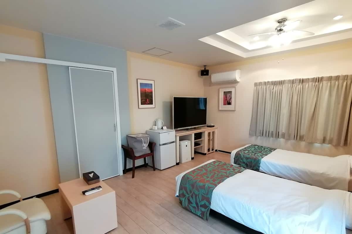 A hotel room with a desk, television, two beds, and a ceiling fan.