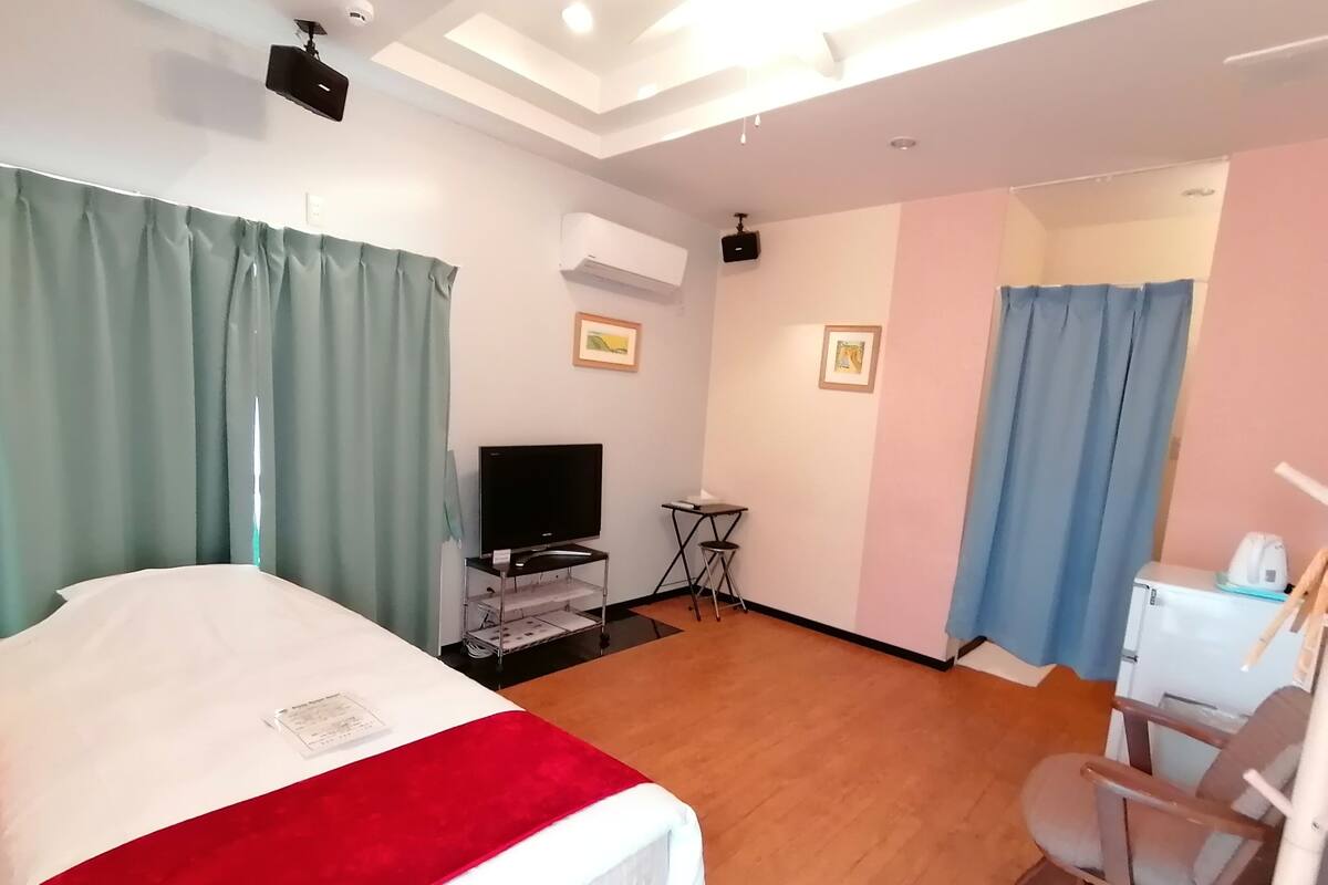 A hotel room with a bed, a desk, a chair, a television, and a kitchenette.