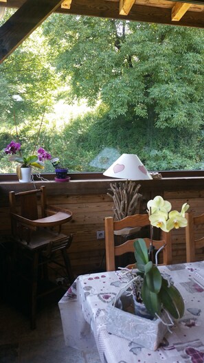 Patio esterno con arredi in legno, un tavolo ricoperto da una tovaglia fantasia e piante in vaso, tra cui orchidee.