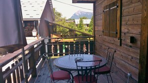 Un patio in legno con un tavolo e sedie rotonde, una ringhiera in legno e una vista su una montagna sullo sfondo.