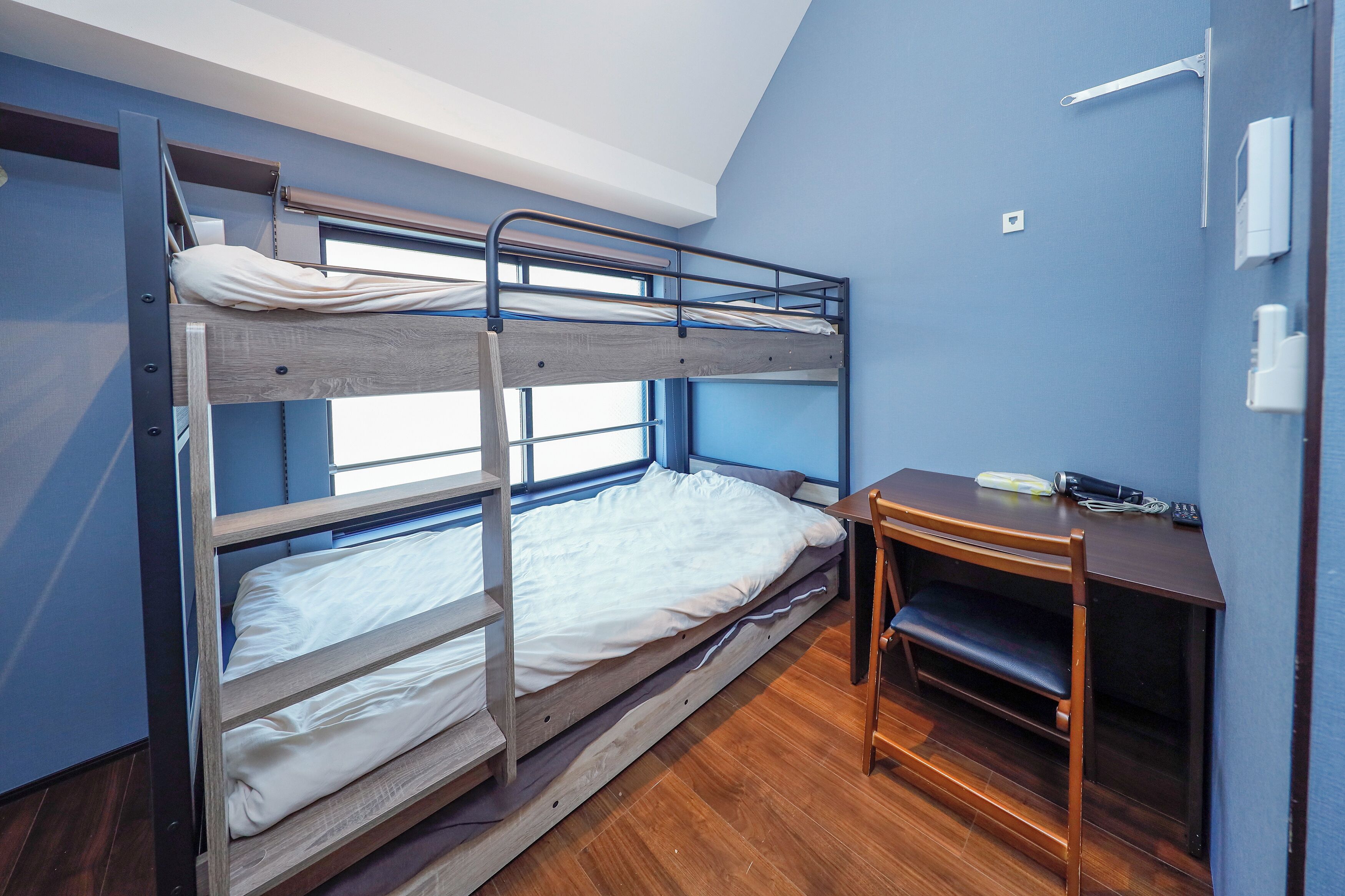 Une chambre avec un lit superposé, un bureau et une chaise, une fenêtre et une porte.
