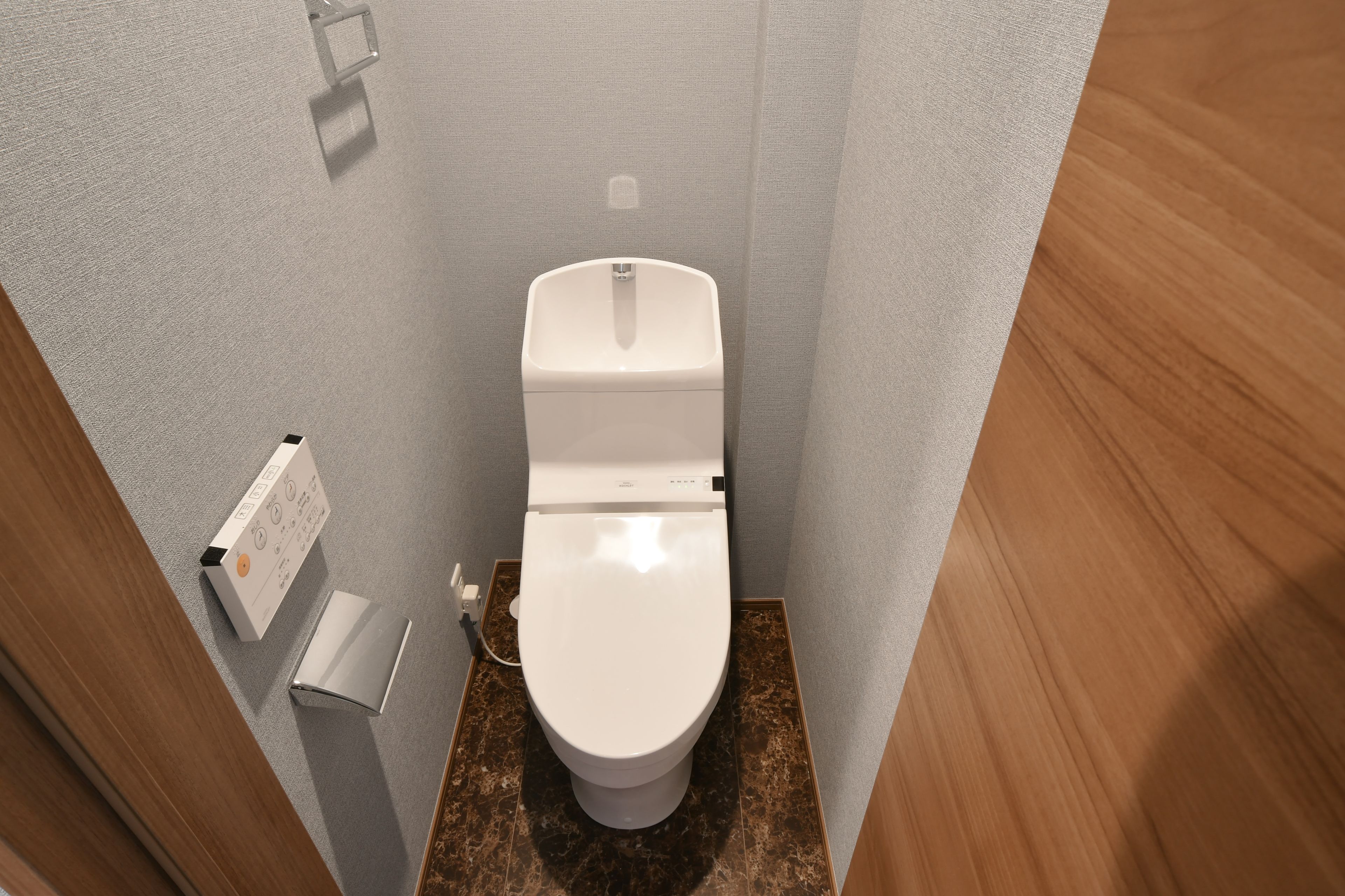 A small bathroom with a white toilet, a paper towel dispenser, and a flush handle.