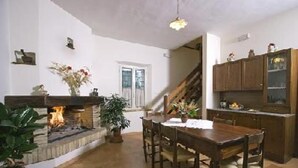 A dining area with a fireplace, wooden dining table, chairs, and a staircase leading to another level. - Canalicchio: Apartment within farmhouse and terrace with Jacuzzi for 4 persons (Canalicchio)