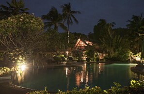 Een resort bij nacht met een zwembad, palmbomen en een verlicht gebouw.