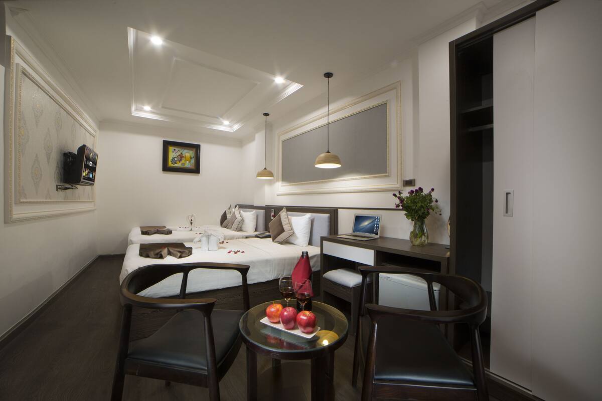 Une chambre d’hôtel avec un lit, un bureau, une chaise, une petite table avec des fruits et un verre de vin, et un téléviseur posé sur le bureau.