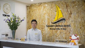 A hotel reception desk with a marble wall, a clock, and a flower vase. - Galliot Central Hotel (Hanoi)