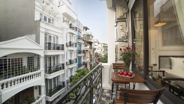 A balcony with a table, chairs, and a vase of flowers. - Galliot Central Hotel (Hanoi)