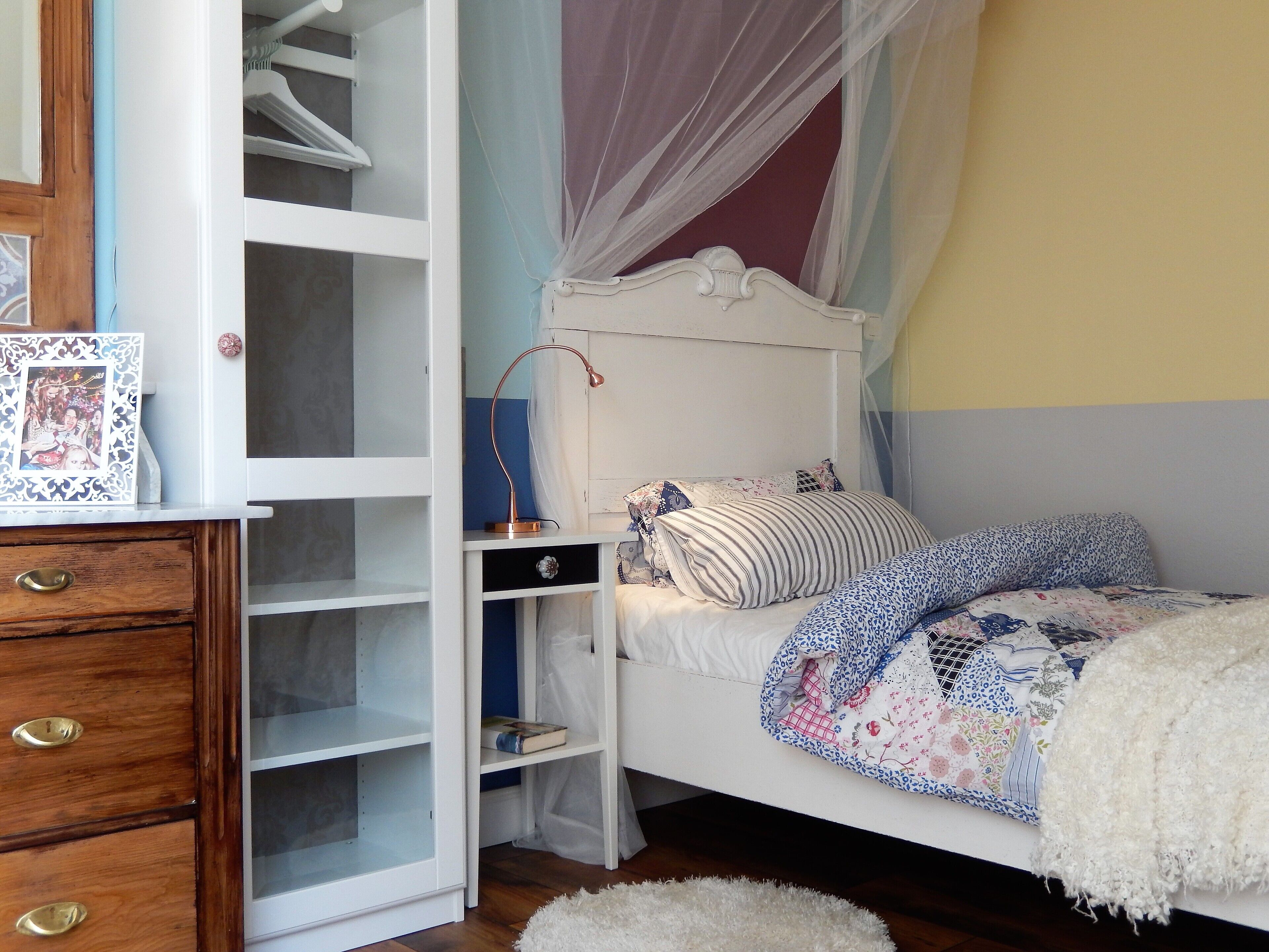 Un dormitorio con una cama blanca, un aparador de madera, un armario y una mesita de noche.