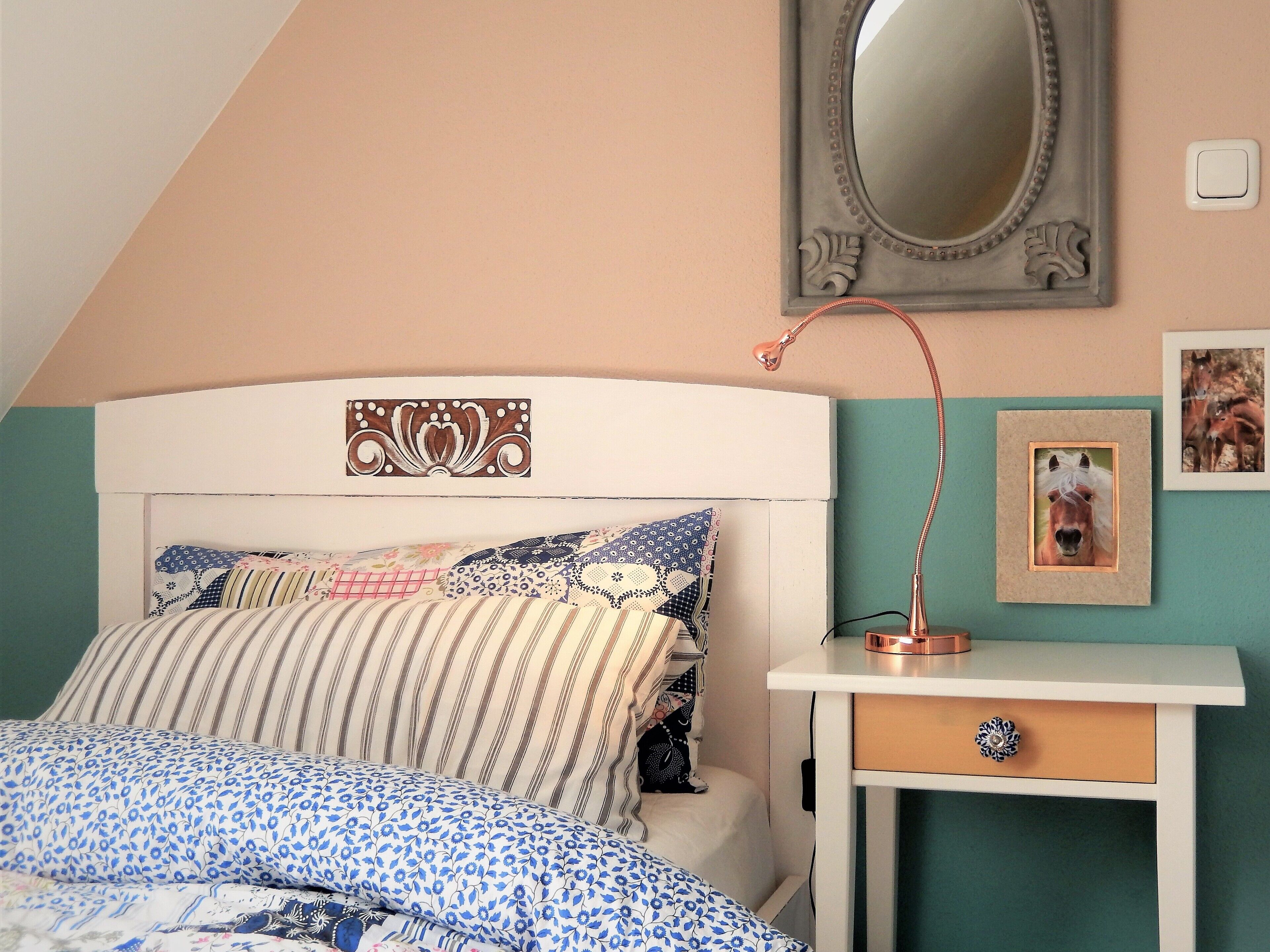 A bedroom with a bed, a bedside table, a mirror, and wall decorations.