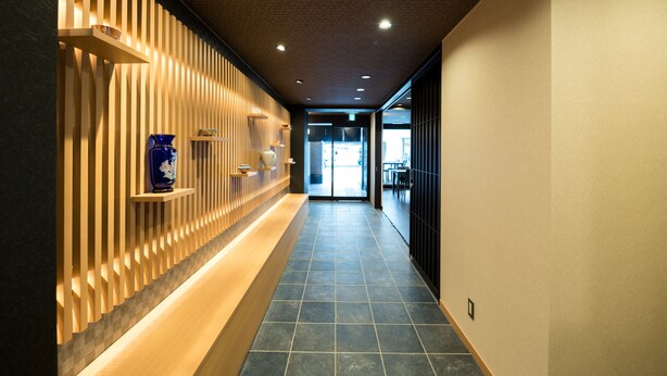 A corridor with a wooden slat wall, a blue vase, and a tiled floor. - Shiki Suites - Kyoto Umekoji (Kyoto)