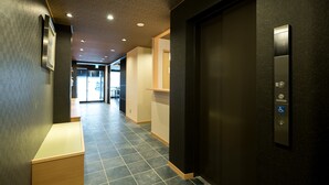A modern hallway with a black elevator, a bench, and a door leading to another room. - Shiki Suites - Kyoto Umekoji (Kyoto)