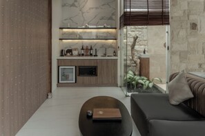 A modern living area with a sofa, a coffee table, a kitchen with marble backsplash, and a stone wall.