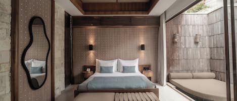 A modern bedroom with a large bed, a bench, a mirror, and a view of a garden.