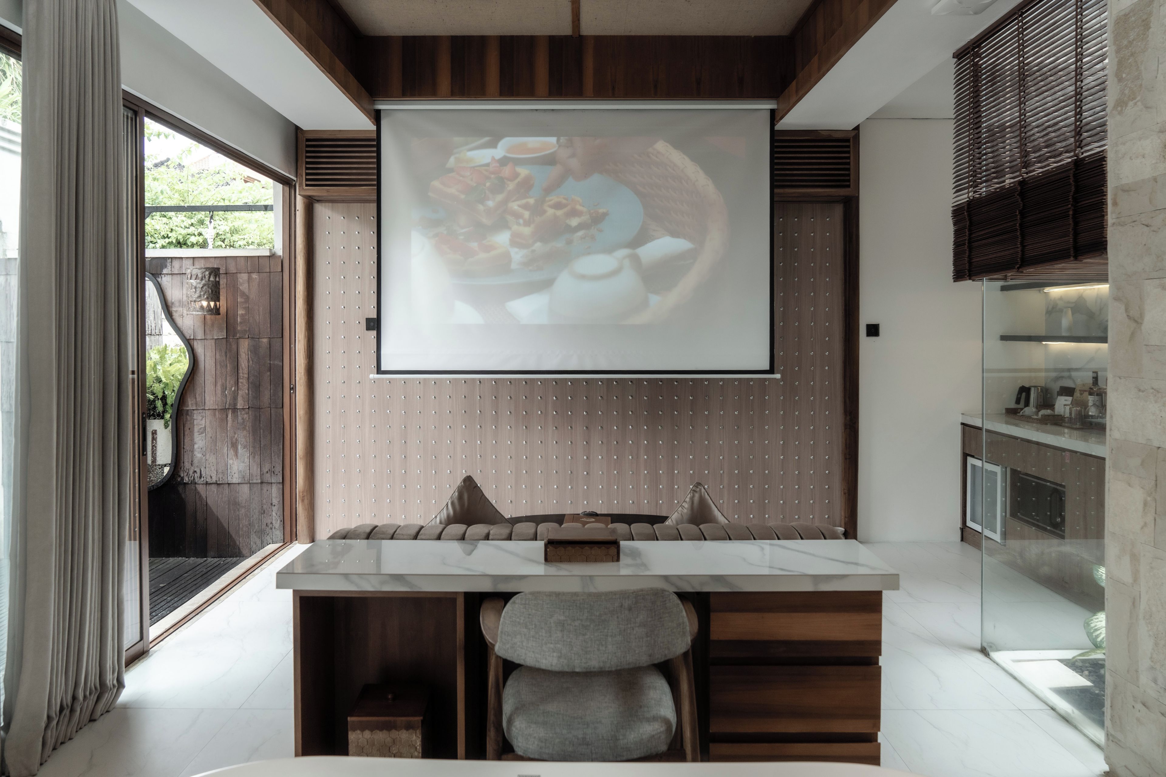 A modern kitchen with a large screen displaying food, a marble countertop, and a seating area with cushions.