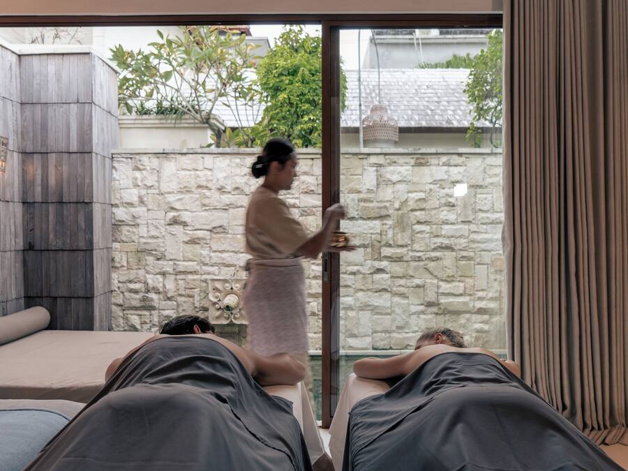 Une salle de spa équipée de deux tables de massage, d’un mur en pierre et offrant une vue sur l’extérieur.