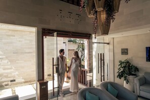 Una coppia in piedi in un interno moderno con una porta vetrata che dà sull'esterno, una sveglia a parete e un cartello con scritto 'INNI VIE HOSPITALITY'.