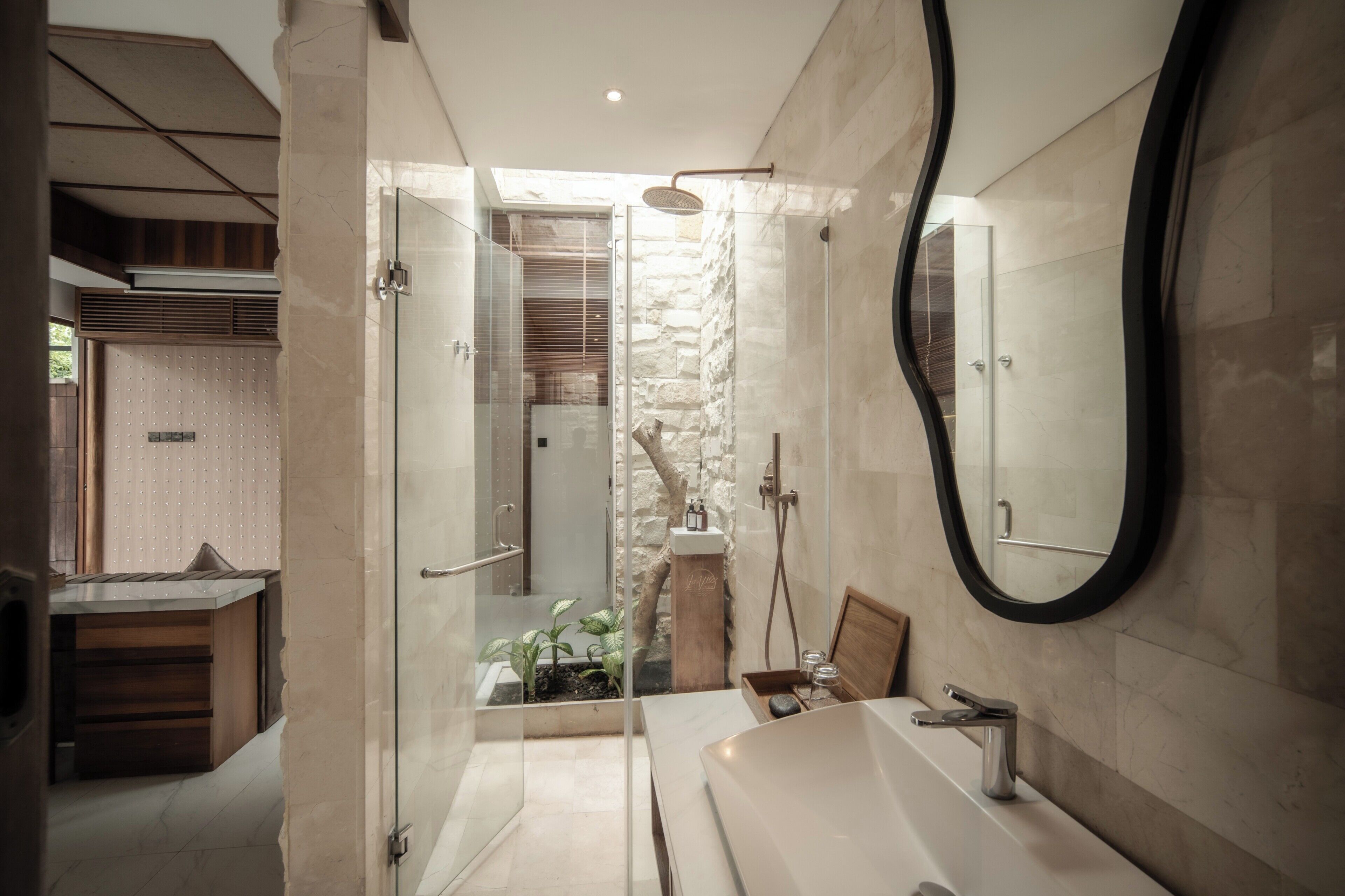 A modern bathroom with a glass-enclosed shower, a large mirror, and a wooden vanity.