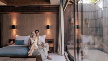 Un dormitorio moderno con una cama grande, mesitas de noche y un separador de vidrio.