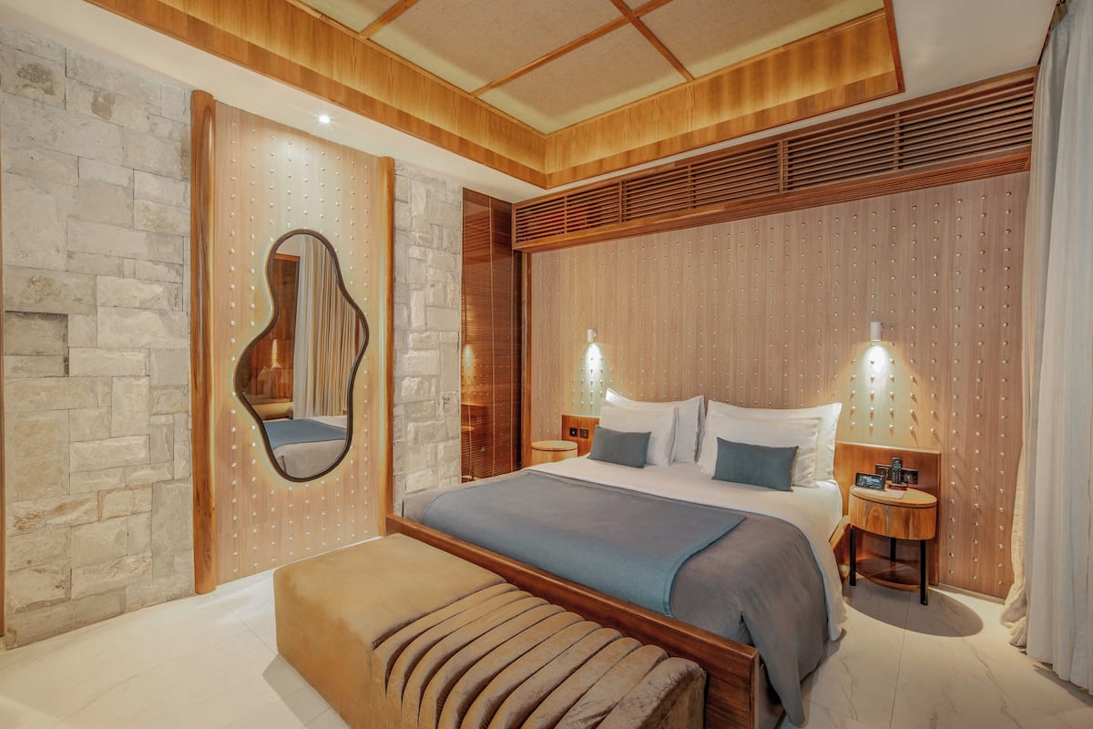 A modern bedroom with a large bed, a wooden headboard, stone wall, and a mirror.