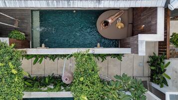 Una piscina al terrat amb una zona d'estar circular i vegetació abundant al voltant.