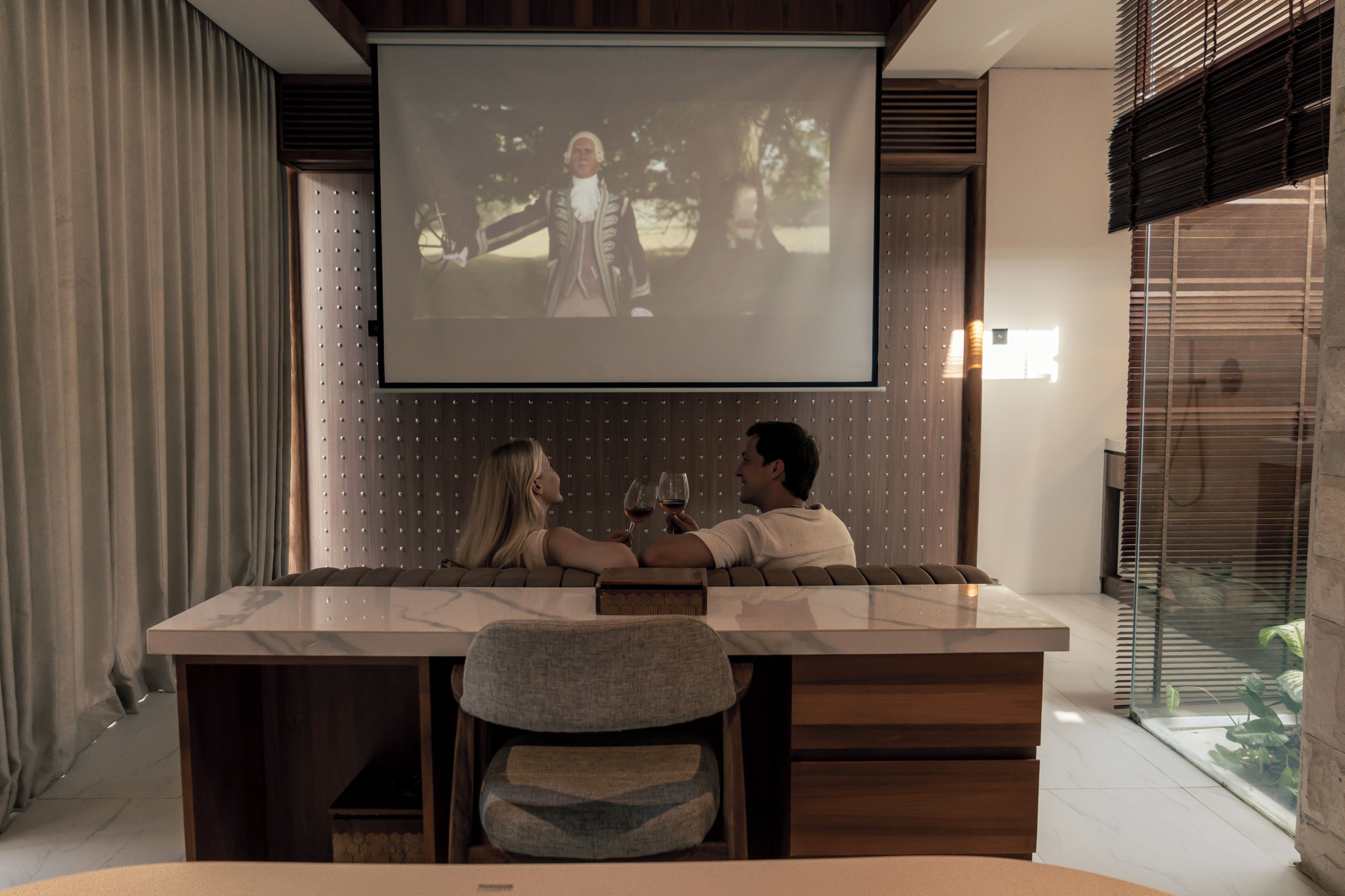 Een moderne woonkamer met een grote flatscreen televisie aan de muur, een eettafel met twee stoelen en een bank.