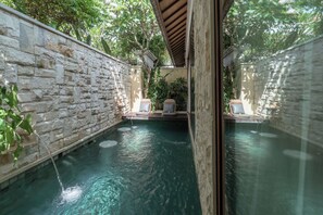 Zona de piscina amb parets de pedra, dues gandules i una piscina blava i cristal·lina.