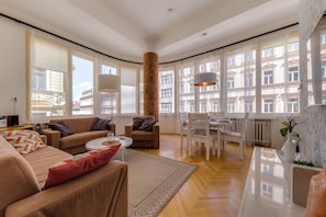 Relax in this spacious living room with a large window offering a city view, comfortable seating, and a dining table.