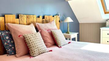 A bedroom with a sloped ceiling, a wooden headboard, a bedside lamp, and a floral-patterned pillow.