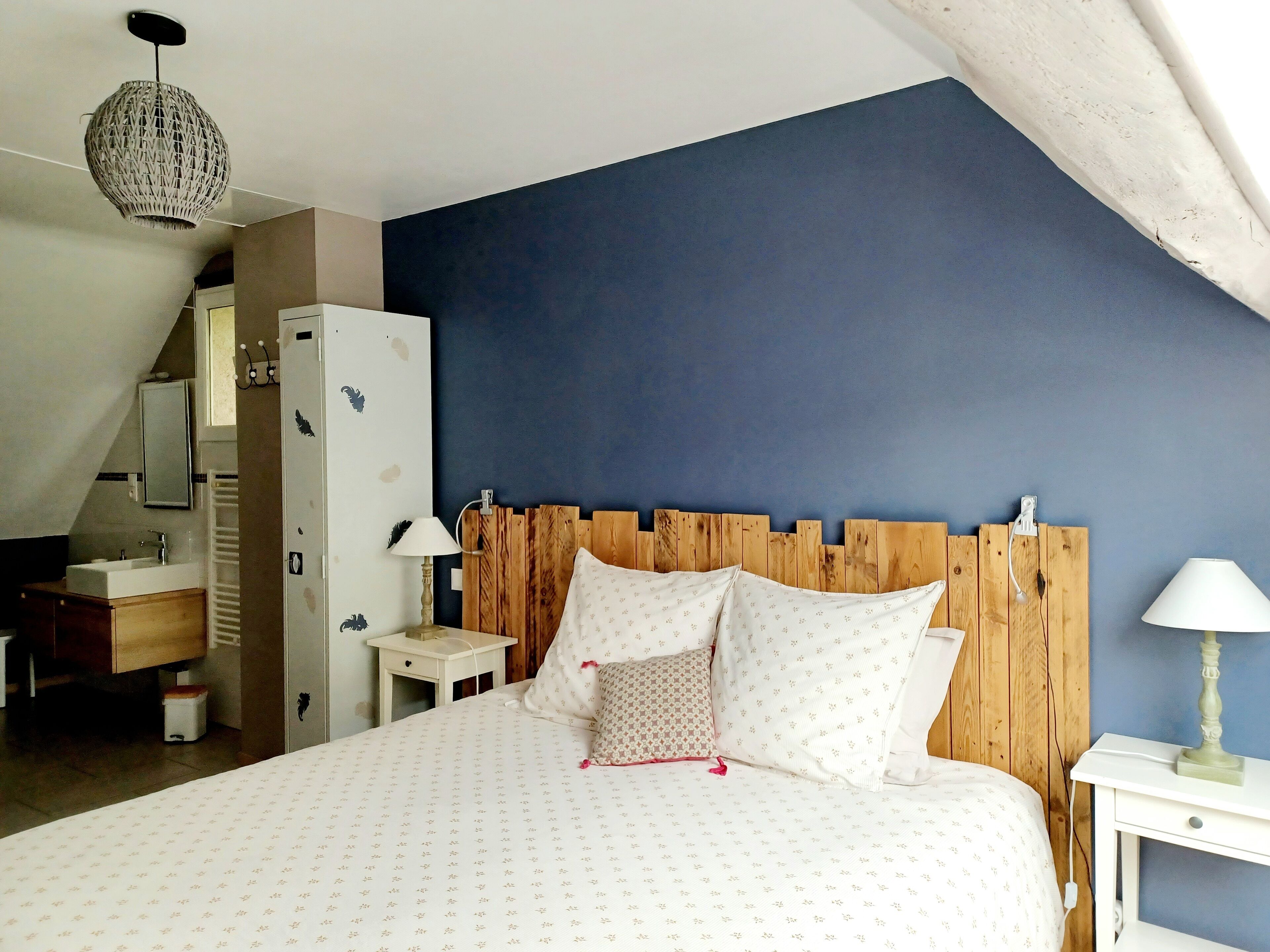 Une chambre à coucher avec une tête de lit en bois, un lit avec une literie à motifs, une table de chevet avec une lampe et une commode avec un miroir.