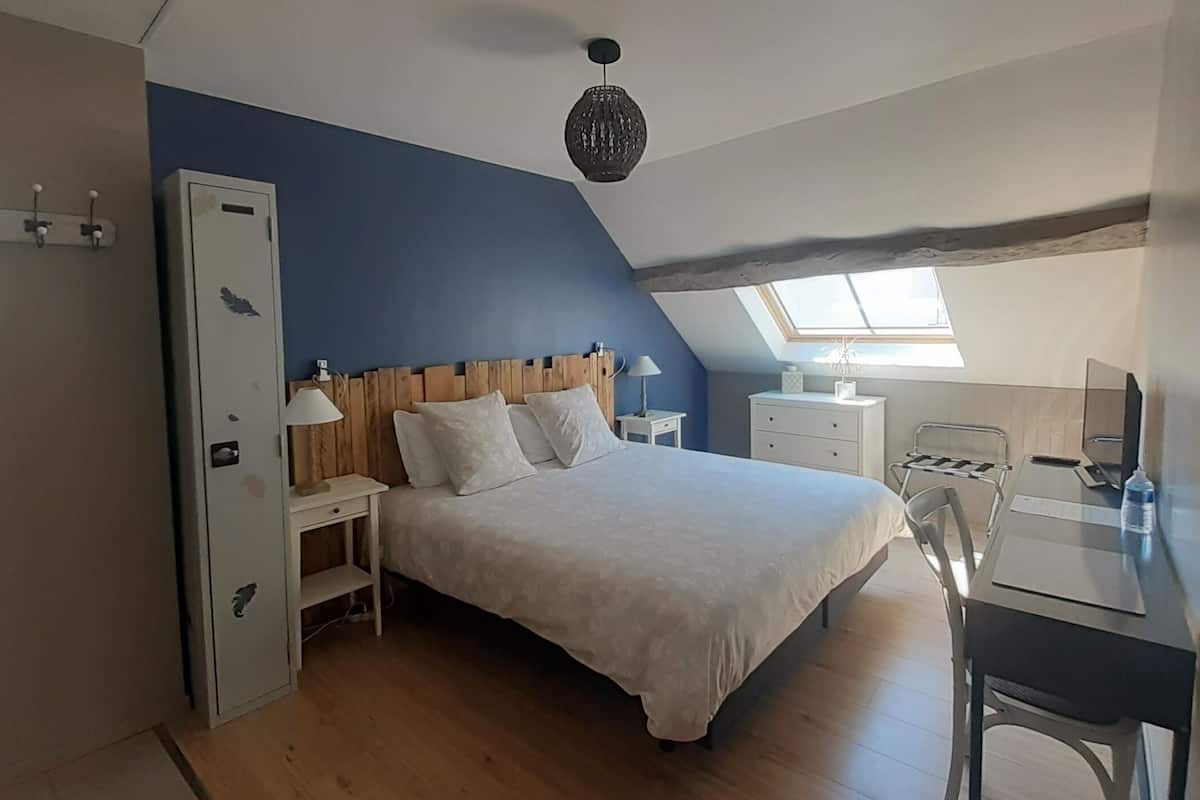 Een slaapkamer met een bed, nachtkastjes, een bureau en een stoel. Er is een raam dat natuurlijk licht binnenlaat en een dakraam boven het bed.