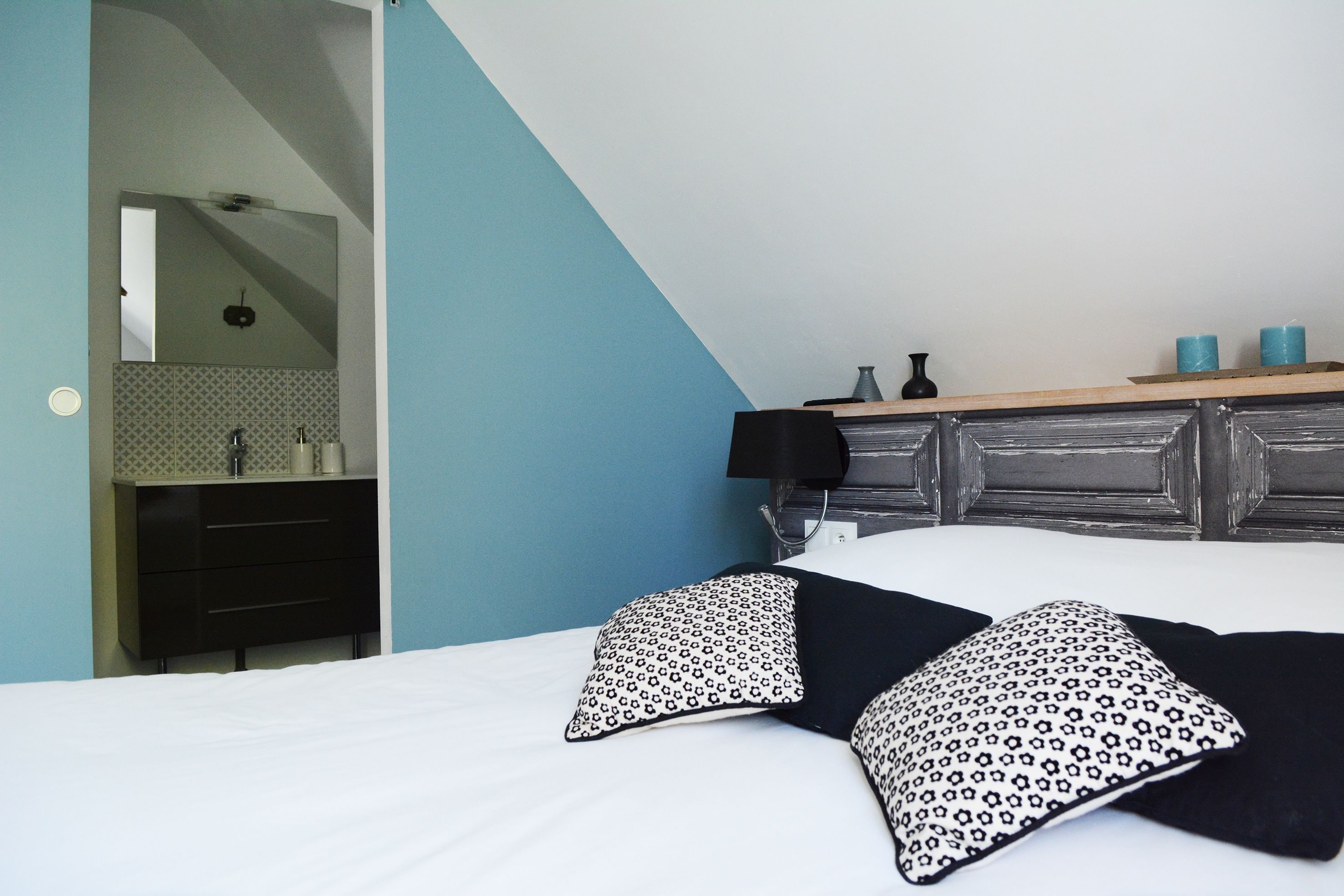 Une chambre à coucher avec un lit, des oreillers, une table de chevet, un miroir et une commode.