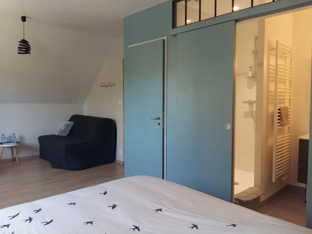 Un dormitorio con cama, un sillón oscuro, un armario y una zona de ducha.