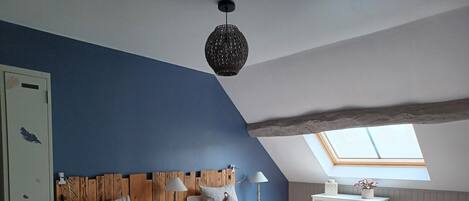 A bedroom with two beds, a skylight, a wooden headboard, a desk, and a chair.