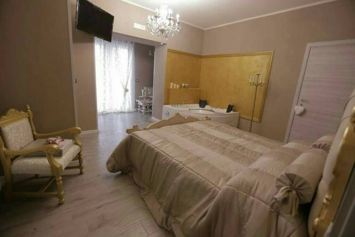 A bedroom with a large bed, a sitting area with a chair, a vanity with a mirror, and a chandelier.