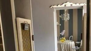 Un couloir mène à une salle à manger agrémentée d’un lustre, d’une table décorée de fleurs et d’une chaise blanche.