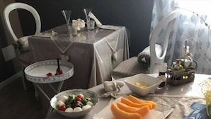 Une table à manger dressée avec différents plats, notamment une salade, des tranches de melon, de la charcuterie et un objet en forme de cœur.