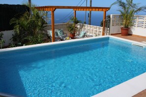 A clear blue pool with a wooden pergola, potted plants, and lounge chairs. - La casa de mi abuela with heatable pool (Garachico)