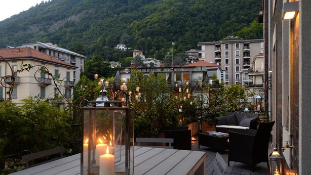Una terraza con mesa de madera, muebles de mimbre y velas en faroles de cristal.