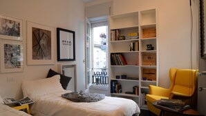 Un dormitorio con cama, estantería, silla y ventana.