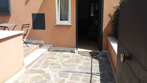 A small outdoor patio with stone flooring, a single window, and a door leading inside. - BB Glicini (Rome)