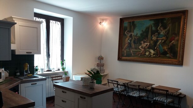 A kitchen with white cabinets, a dining area with a table and chairs, and a large painting on the wall. - BB Glicini (Rome)