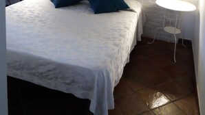 A bedroom with a white brick wall, a bed with a white bedspread and two blue pillows, two bedside lamps, and a small white table with a chair. - BB Glicini (Rome)