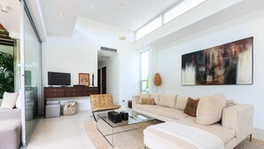 Una sala de estar moderna con una mesa de centro de vidrio, un sofá color beige y un cuadro abstracto grande en la pared.