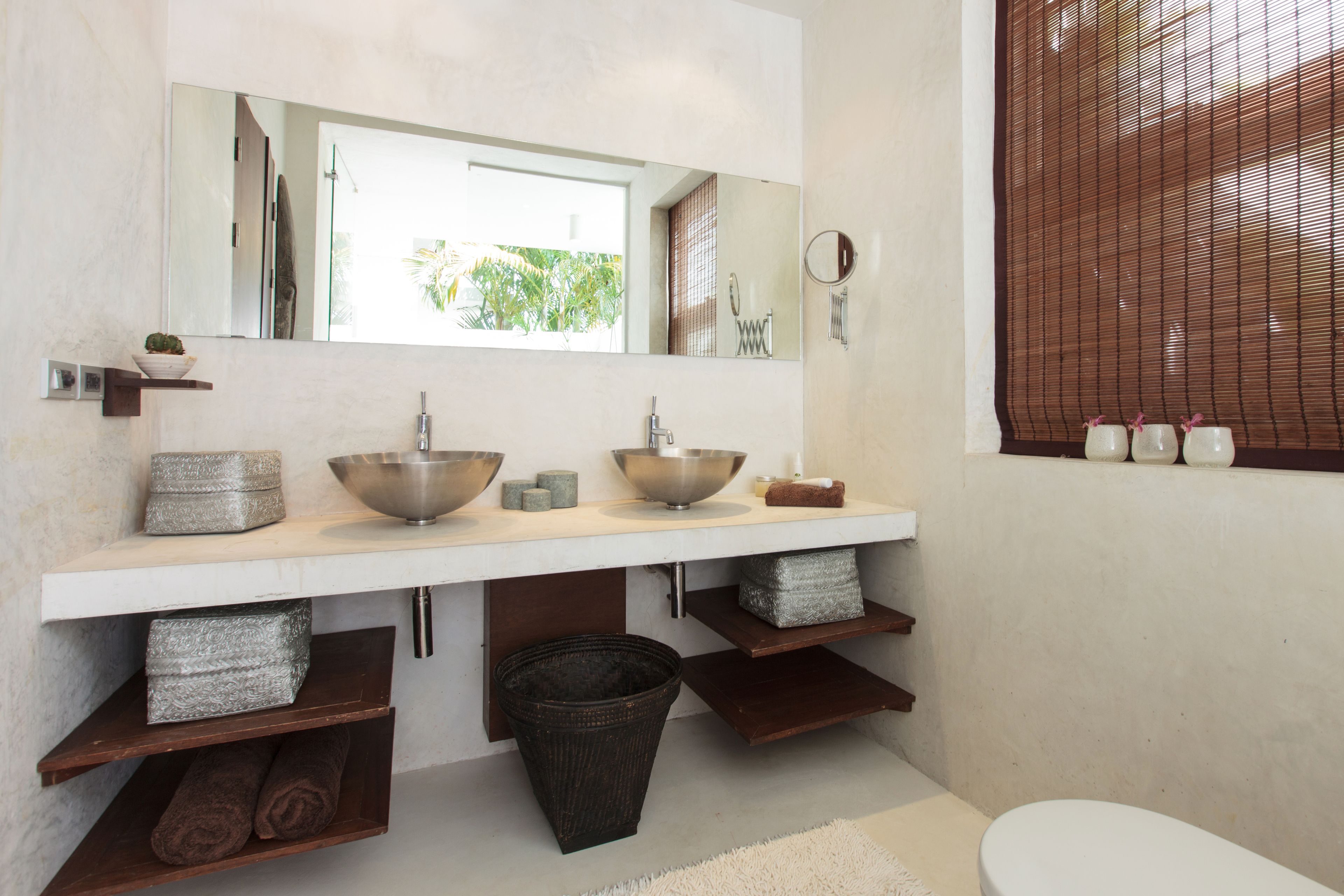 Een badkamer met een grote spiegel, twee wastafels, een toilet en een raam met luxaflex.