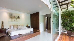 Un dormitorio moderno con una cama grande, una plataforma de madera, una puerta de cristal que da a un balcón y una planta de gran tamaño.